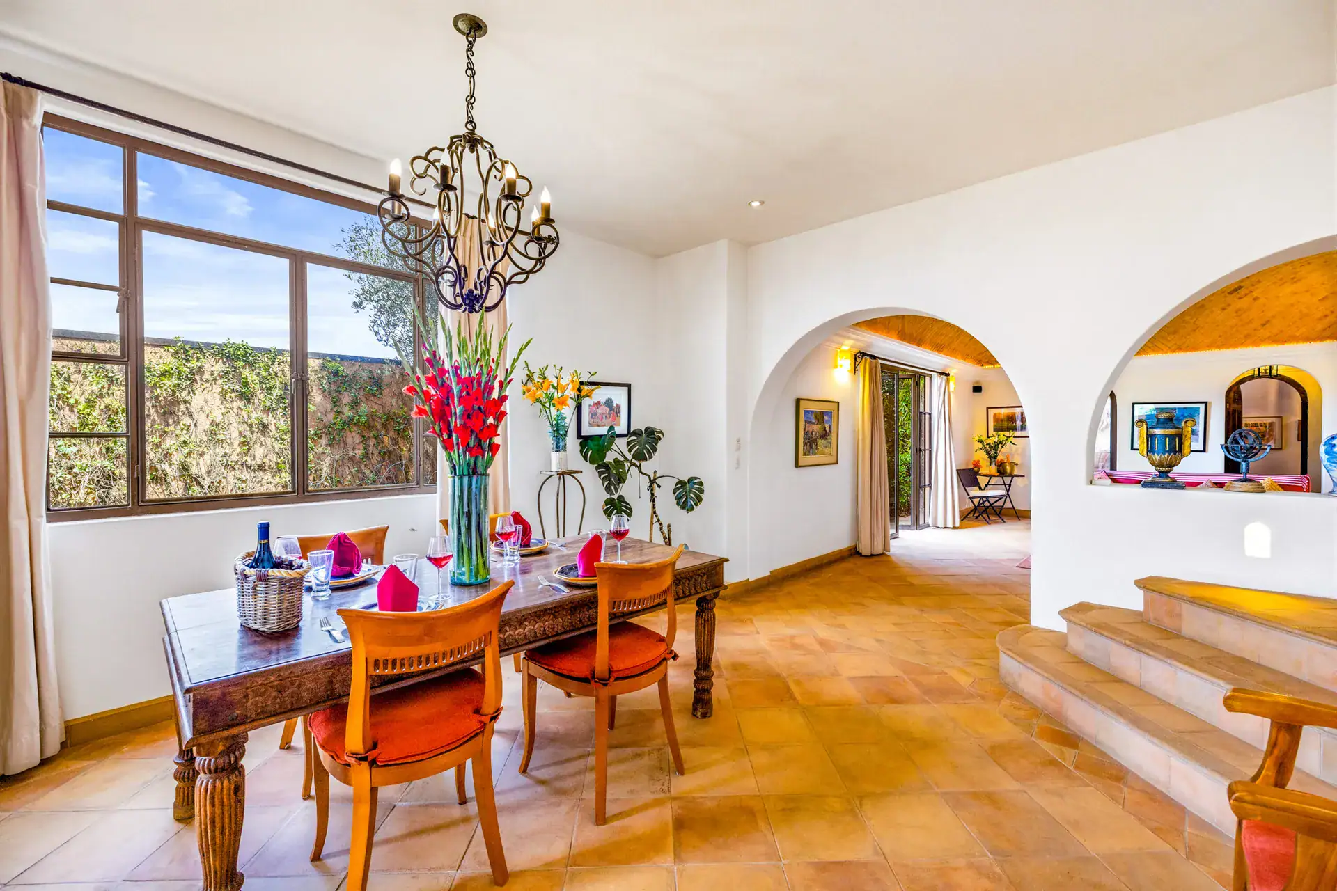 Casa Cascada, dining room with a wood table set for four, orange chairs, a chandelier and windows to the hills, San Miguel de Allende