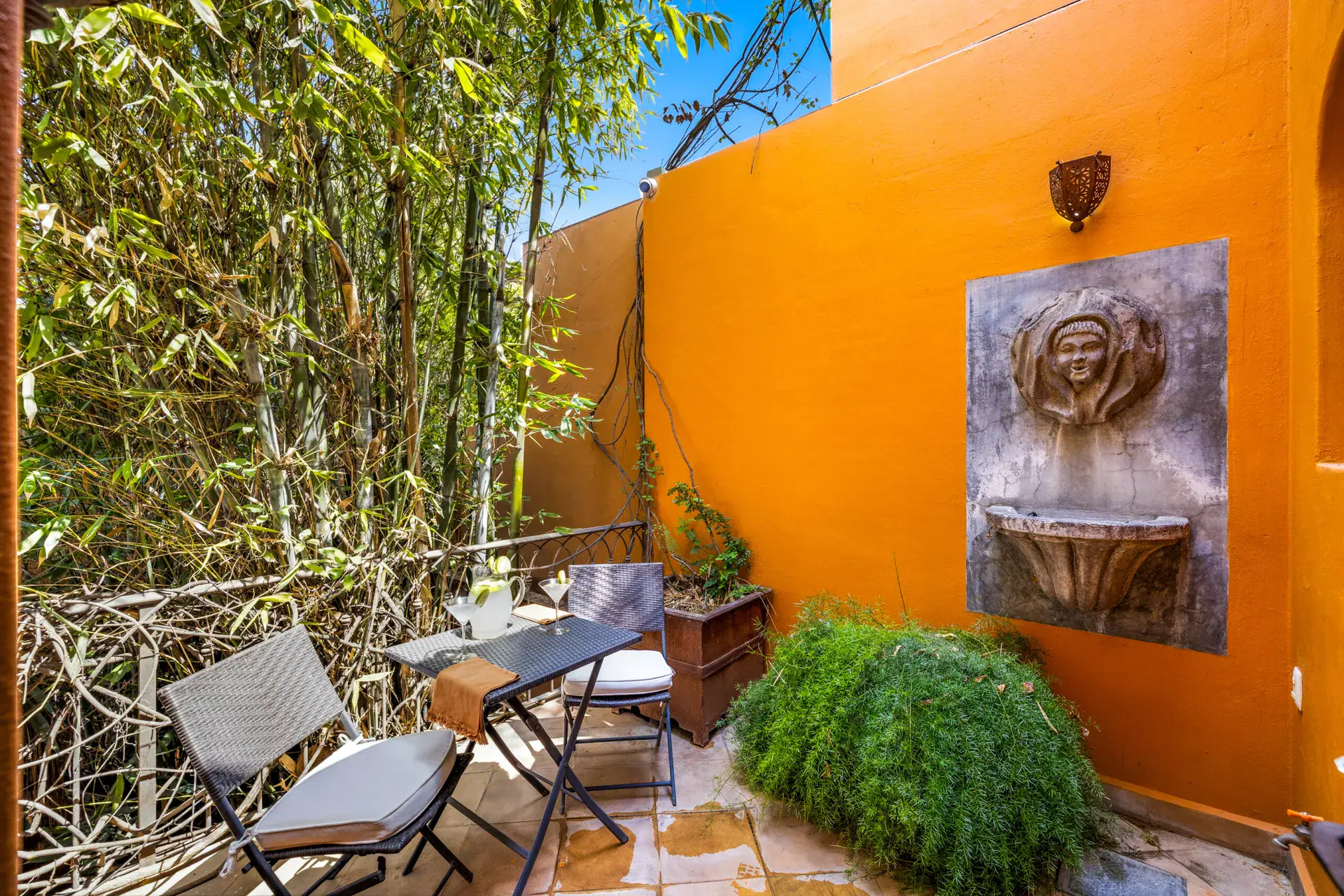Casa Cascada, side terrace with a fountain relief on an orange wall, a bistro table and a bamboo hedge, San Miguel de Allende