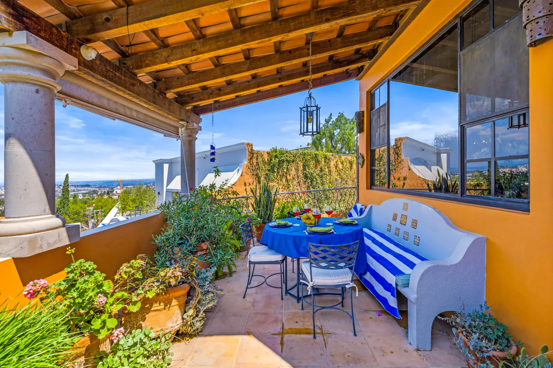 Casa Cascada, covered terrace dining table with a blue cloth, a blue and white bench and a valley view, San Miguel de Allende