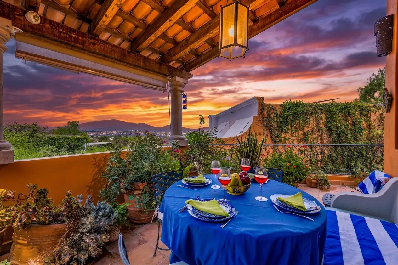 Casa Cascada, terrace dining table at dusk with a blue cloth, striped cushions and a lit sky, San Miguel de Allende