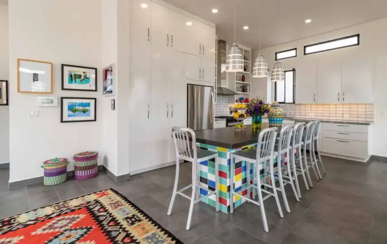 Casa Cielo Abierto, kitchen with white cabinets, a colorful tile-front island with white bar stools and a red kilim rug, San Miguel de Allende