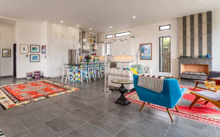 Casa Cielo Abierto, open-plan living area with a white tufted sofa, a blue armchair, a slate fireplace and a colorful kitchen island, San Miguel de Allende
