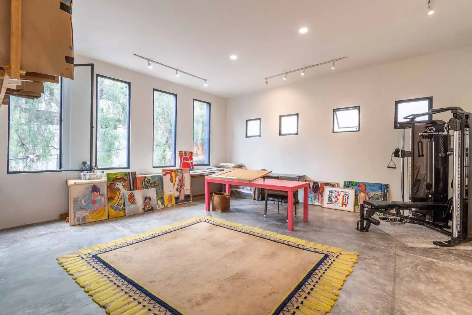Casa Cielo Abierto, studio with a pink table, a weight machine, canvases on the floor and a yellow-fringed rug, San Miguel de Allende