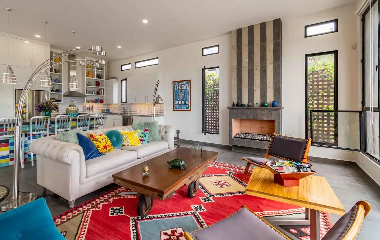 Casa Cielo Abierto, living room with a white sofa, a slate fireplace and an open kitchen with colorful shelves, San Miguel de Allende