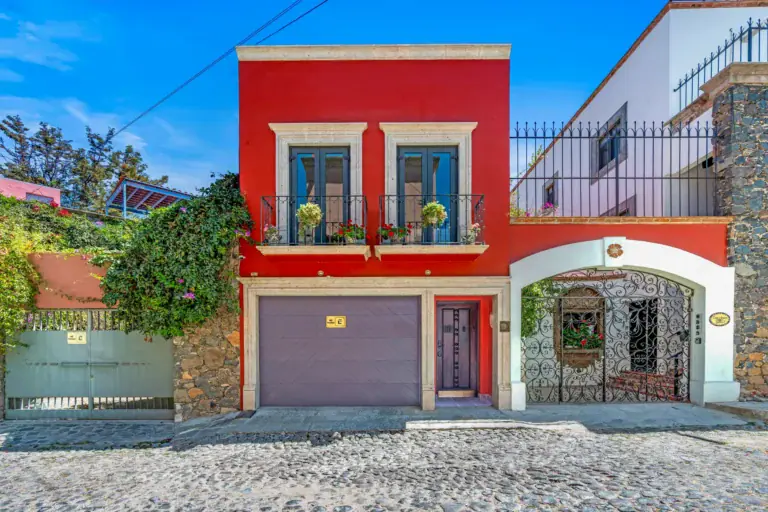 Casa Cleo Petra, red stucco facade with balconies and an arched gate on a cobblestone street, San Miguel de Allende