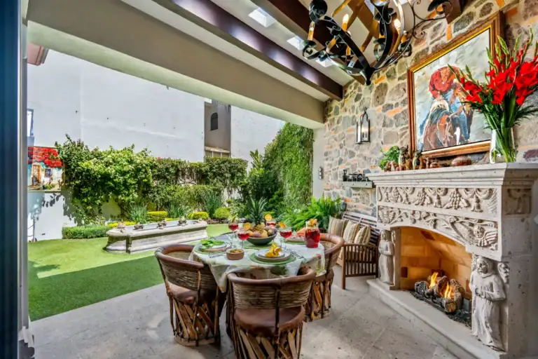 Casa Cleo Petra, covered patio with a carved stone fireplace and a round dining table, San Miguel de Allende