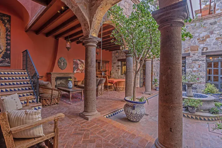 Casa Colonial, courtyard with stone columns, a brick floor and a stair up to an orange loggia, San Miguel de Allende
