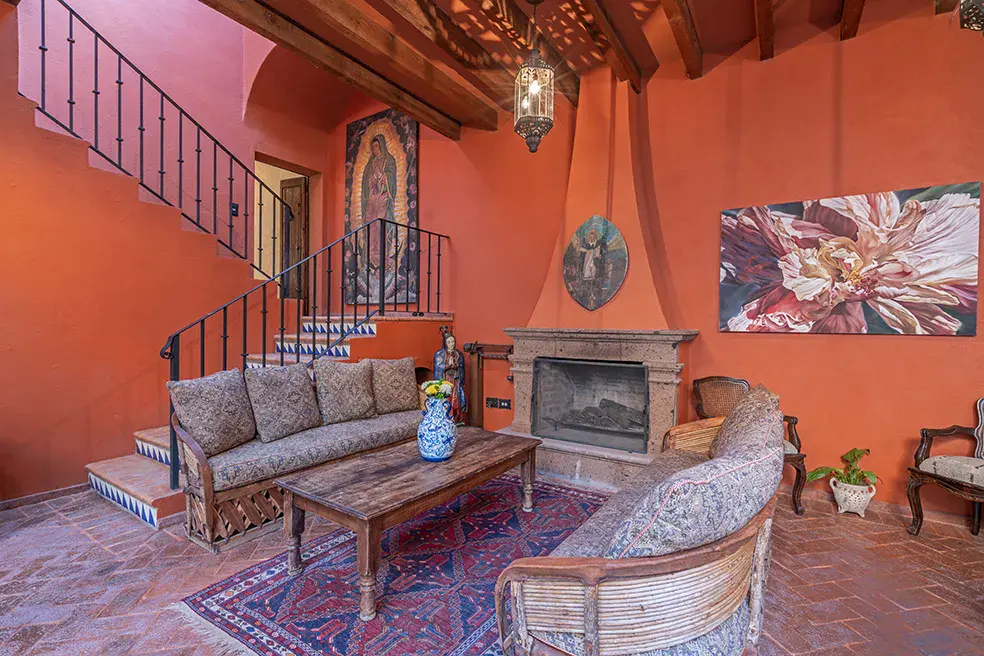 Casa Colonial, orange living room with a corner fireplace, patterned sofas and a stair railing, San Miguel de Allende
