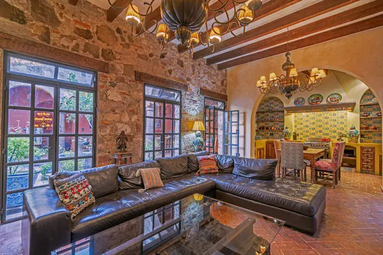 Casa Colonial, living room with a black leather sectional, stone walls and a view to the kitchen, San Miguel de Allende