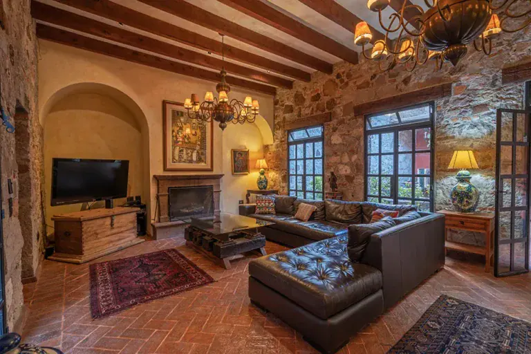 Casa Colonial, living room with a stone wall, a fireplace and a leather sectional under a beamed ceiling, San Miguel de Allende