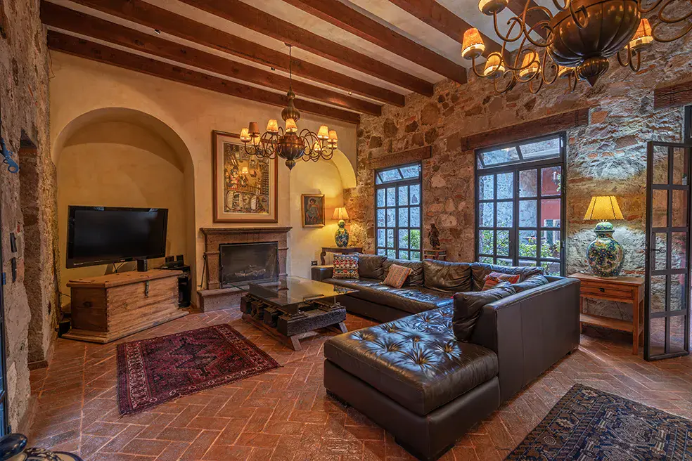 Casa Colonial, living room with a stone wall, a fireplace and a leather sectional under a beamed ceiling, San Miguel de Allende