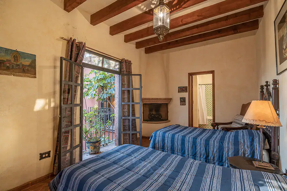Casa Colonial, bedroom with two beds, blue striped bedding and a corner fireplace, San Miguel de Allende