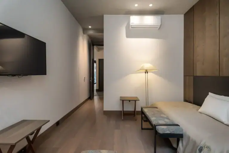 Casa Core, bedroom suite with a wall-mounted television, bench and a hallway beyond, San Miguel de Allende