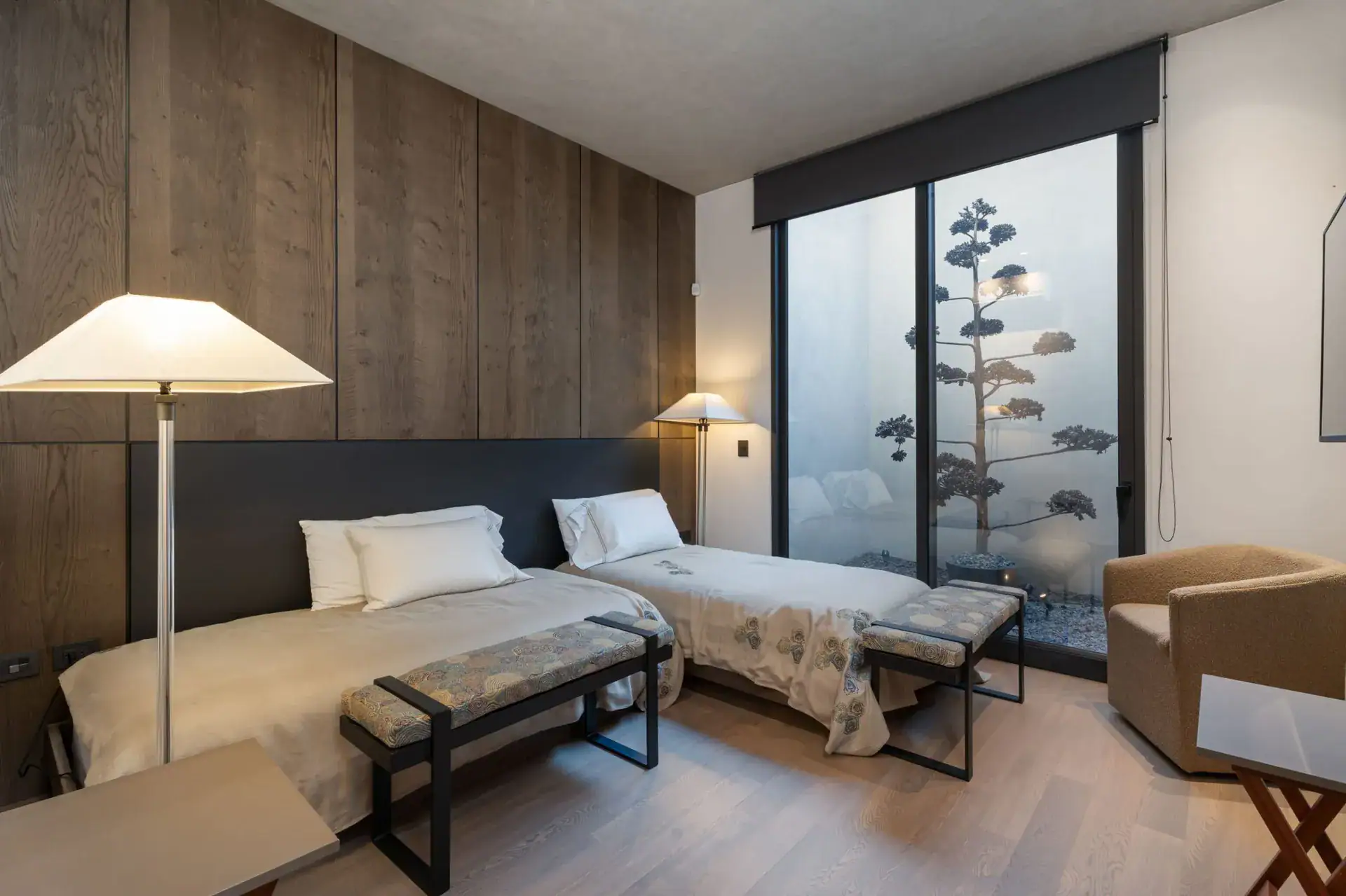 Casa Core, twin-bed bedroom with a wood-paneled wall and a window onto a tall plant, San Miguel de Allende