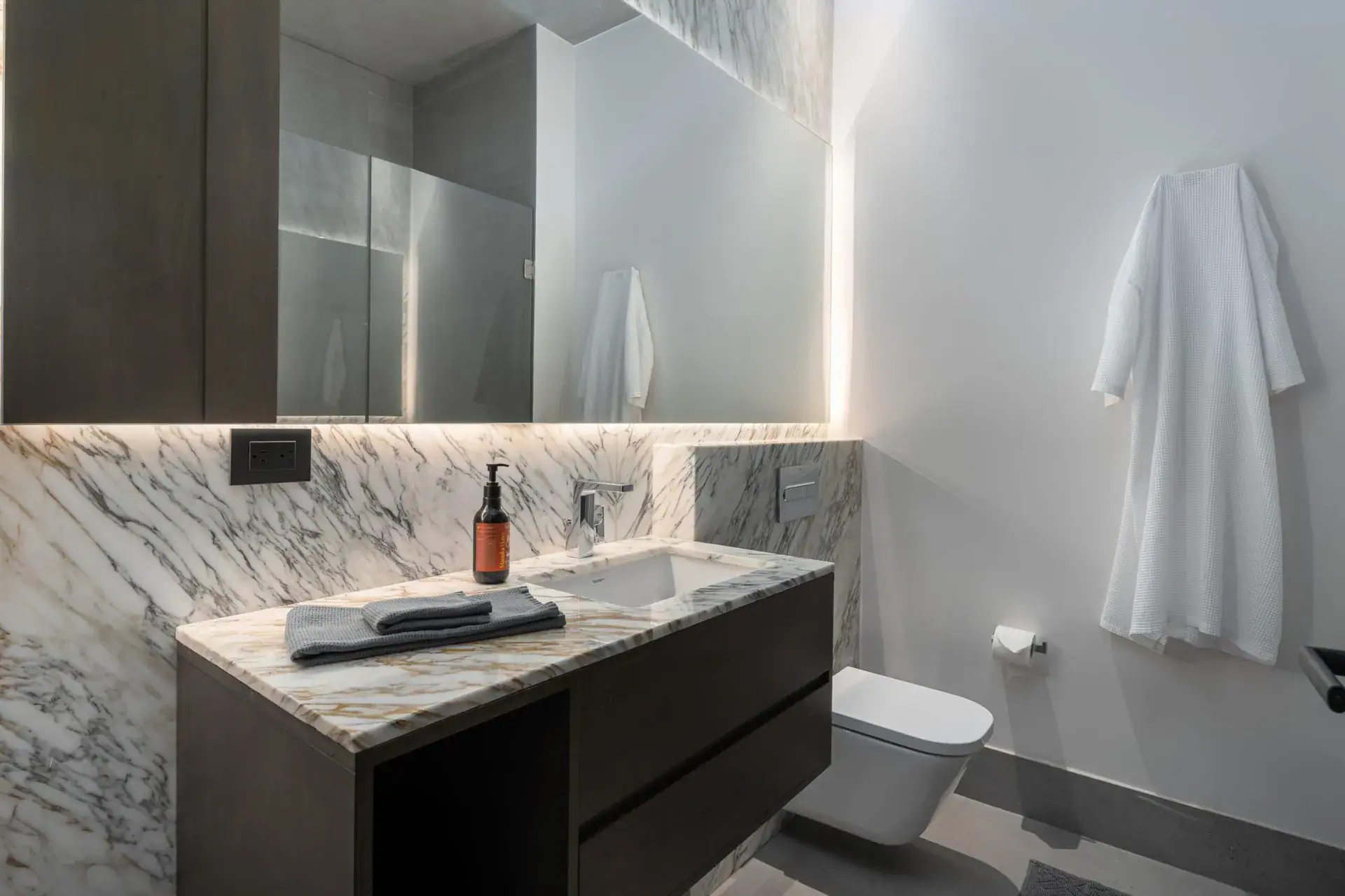 Casa Core, bathroom with a marble vanity, white robe and a wall-hung toilet, San Miguel de Allende