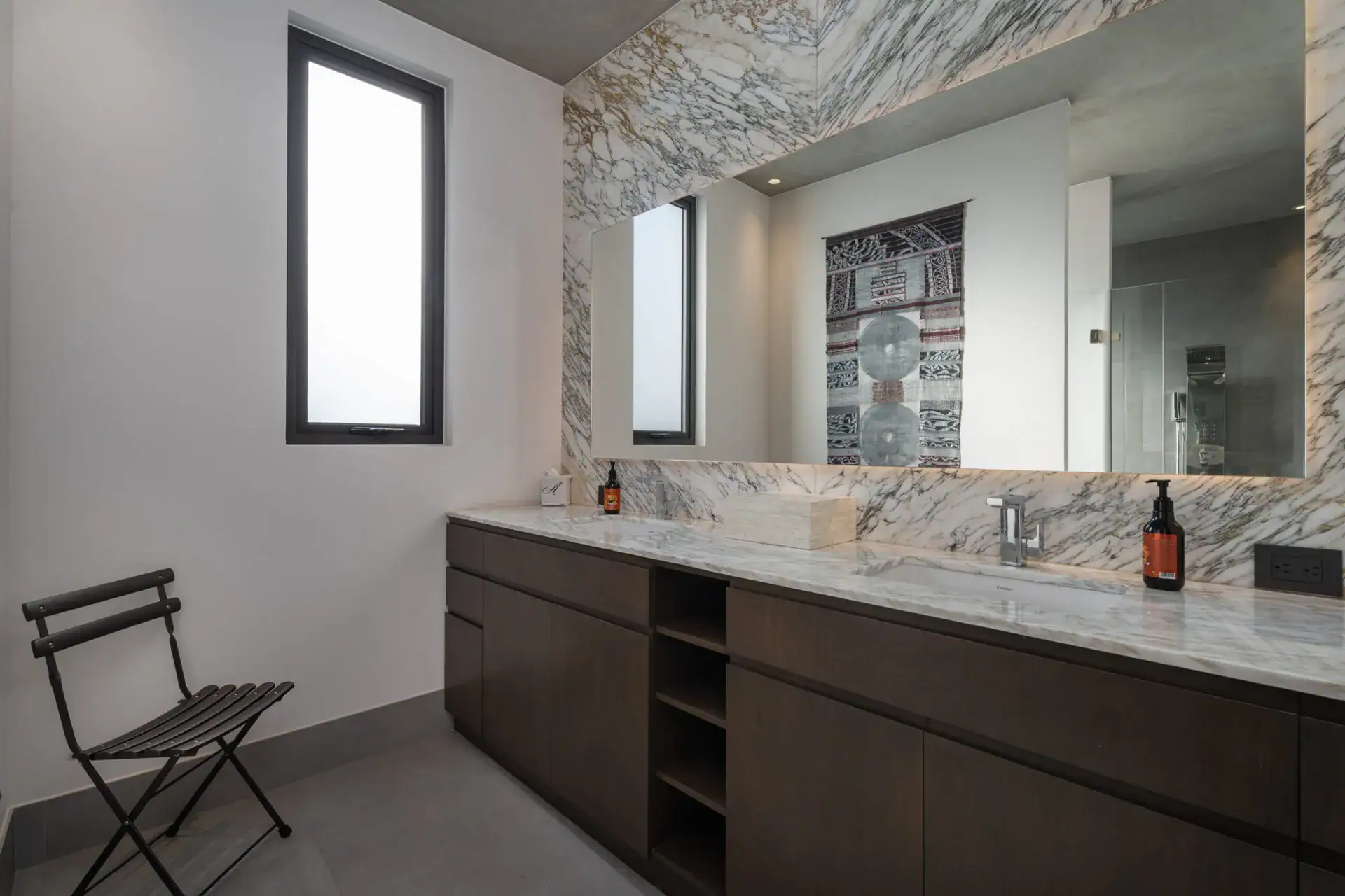 Casa Core, bathroom with a long marble vanity, a wood cabinet and a tall narrow window, San Miguel de Allende