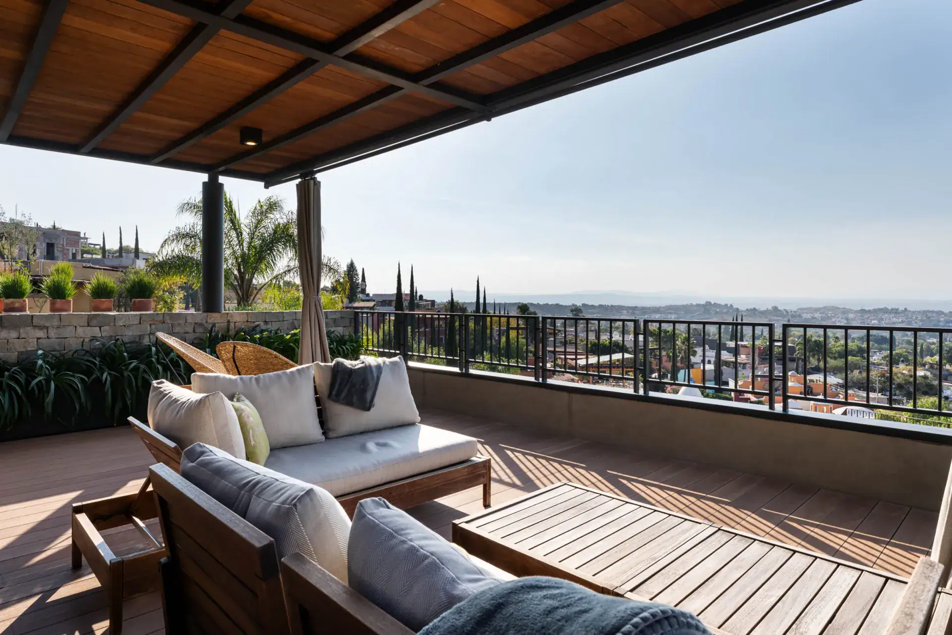 Casa Core, rooftop terrace with outdoor sofas under a wood-slat roof and a city view, San Miguel de Allende