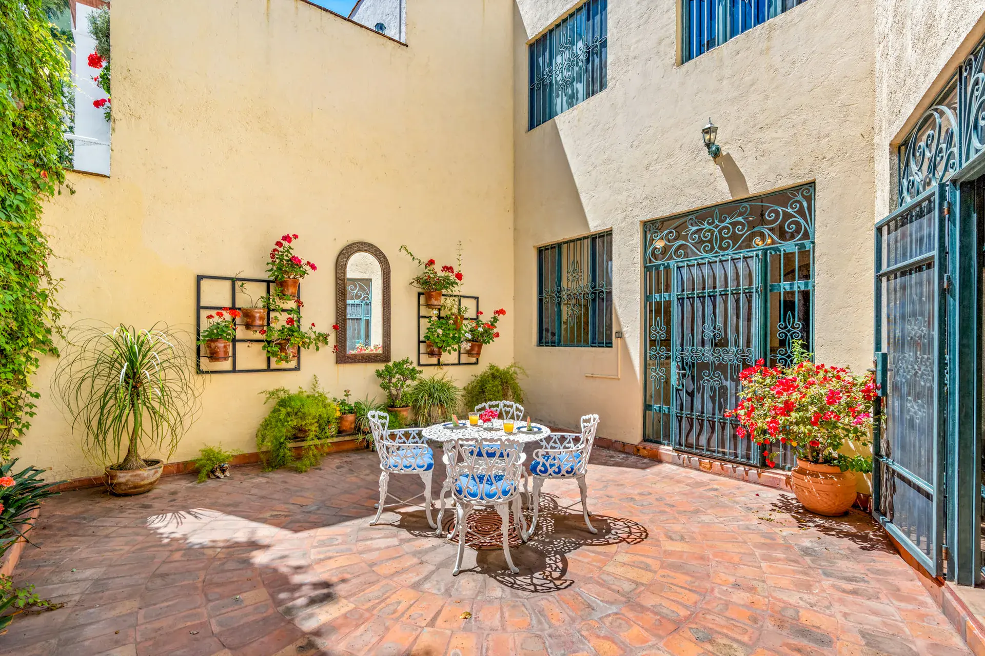 Casa Cul-De-Sac Armonia, courtyard with a bistro set, flower pots, a wall of climbing plants and a mirror on the pale yellow wall, San Miguel de Allende