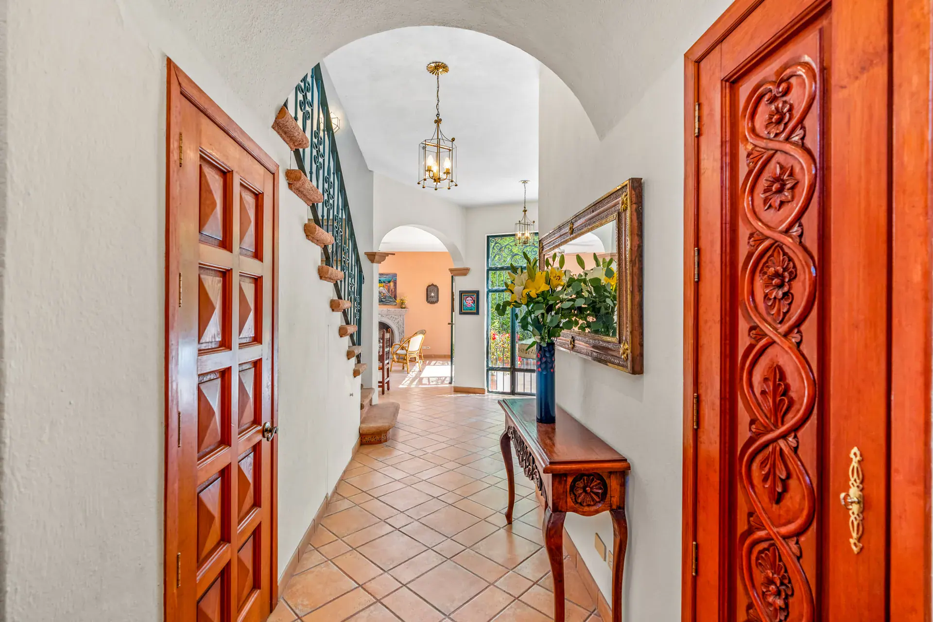 Casa Cul-De-Sac Armonia, entry hall with a carved red wood door, a console with a mirror and flowers and a staircase, San Miguel de Allende