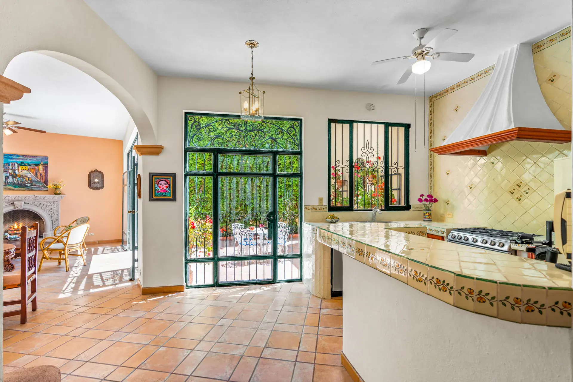 Casa Cul-De-Sac Armonia, kitchen with a hand-painted tile counter, a white range hood, a gas range and a view to the fireplace room, San Miguel de Allende