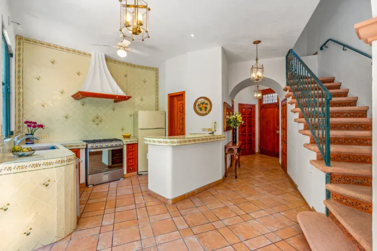 Casa Cul-De-Sac Armonia, kitchen with painted tile counters, a stainless range, a white refrigerator and a stair with a teal iron railing, San Miguel de Allende