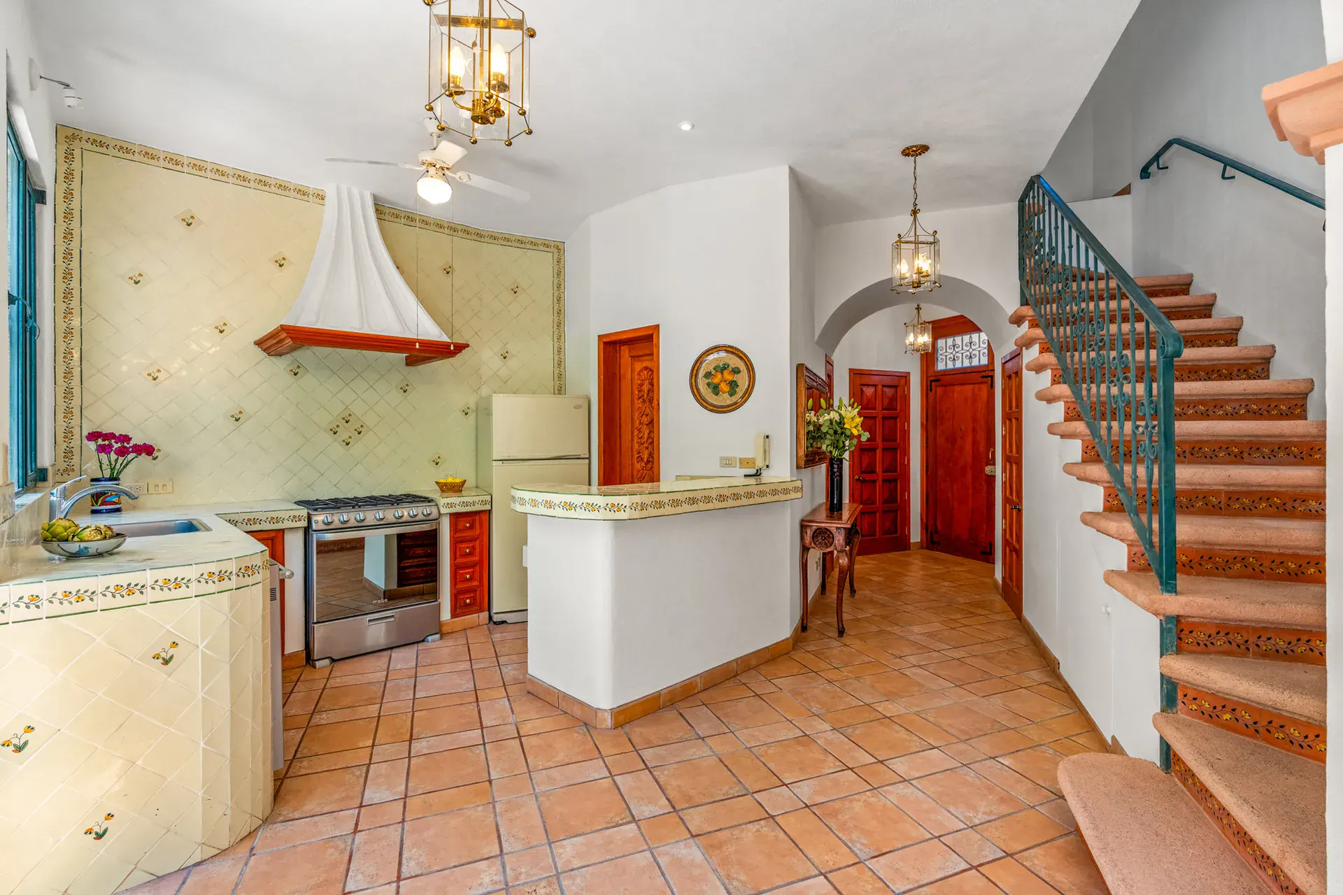 Casa Cul-De-Sac Armonia, kitchen with painted tile counters, a stainless range, a white refrigerator and a stair with a teal iron railing, San Miguel de Allende