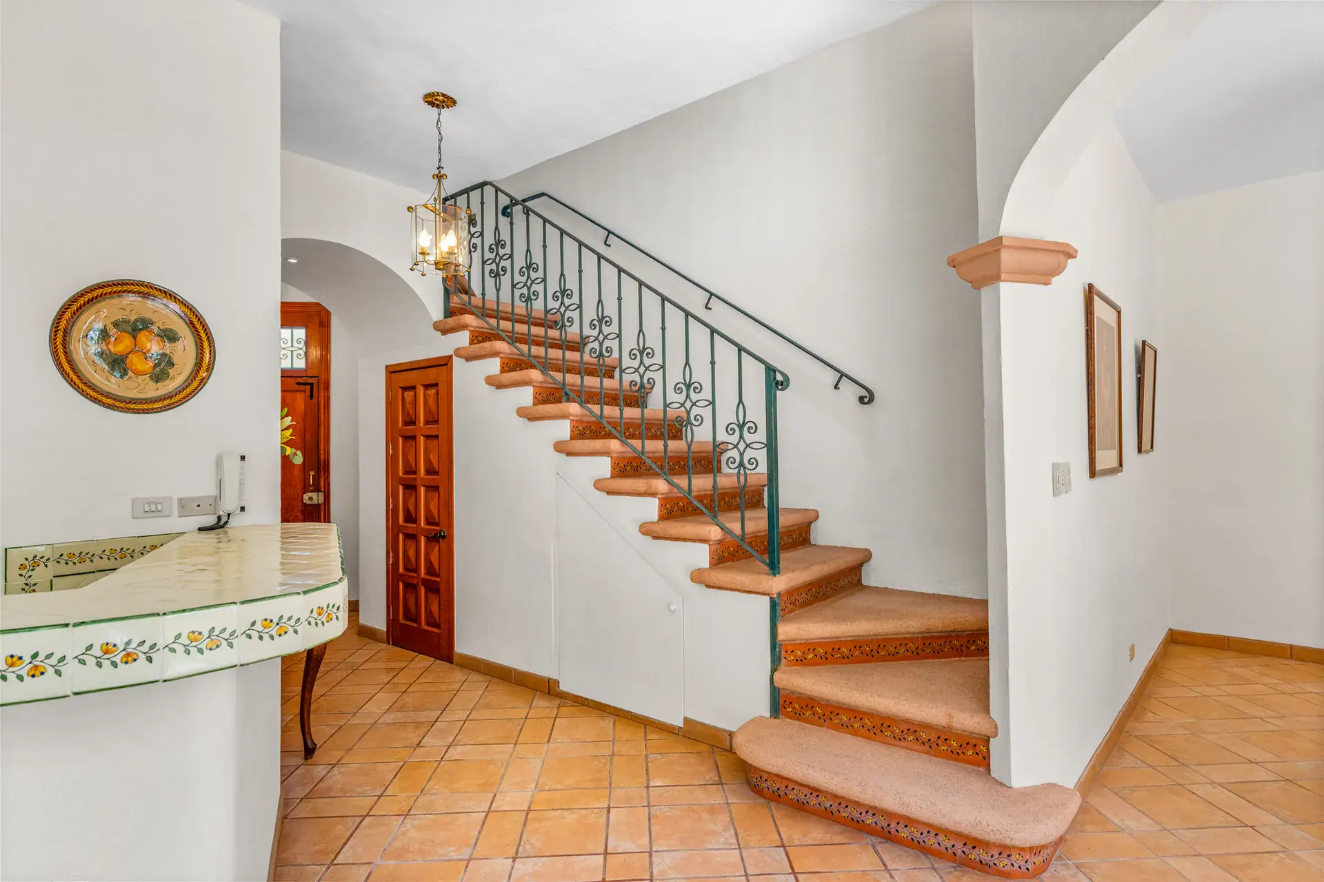 Casa Cul-De-Sac Armonia, staircase with a teal iron railing and carved terracotta steps beside a tile counter and an arch, San Miguel de Allende