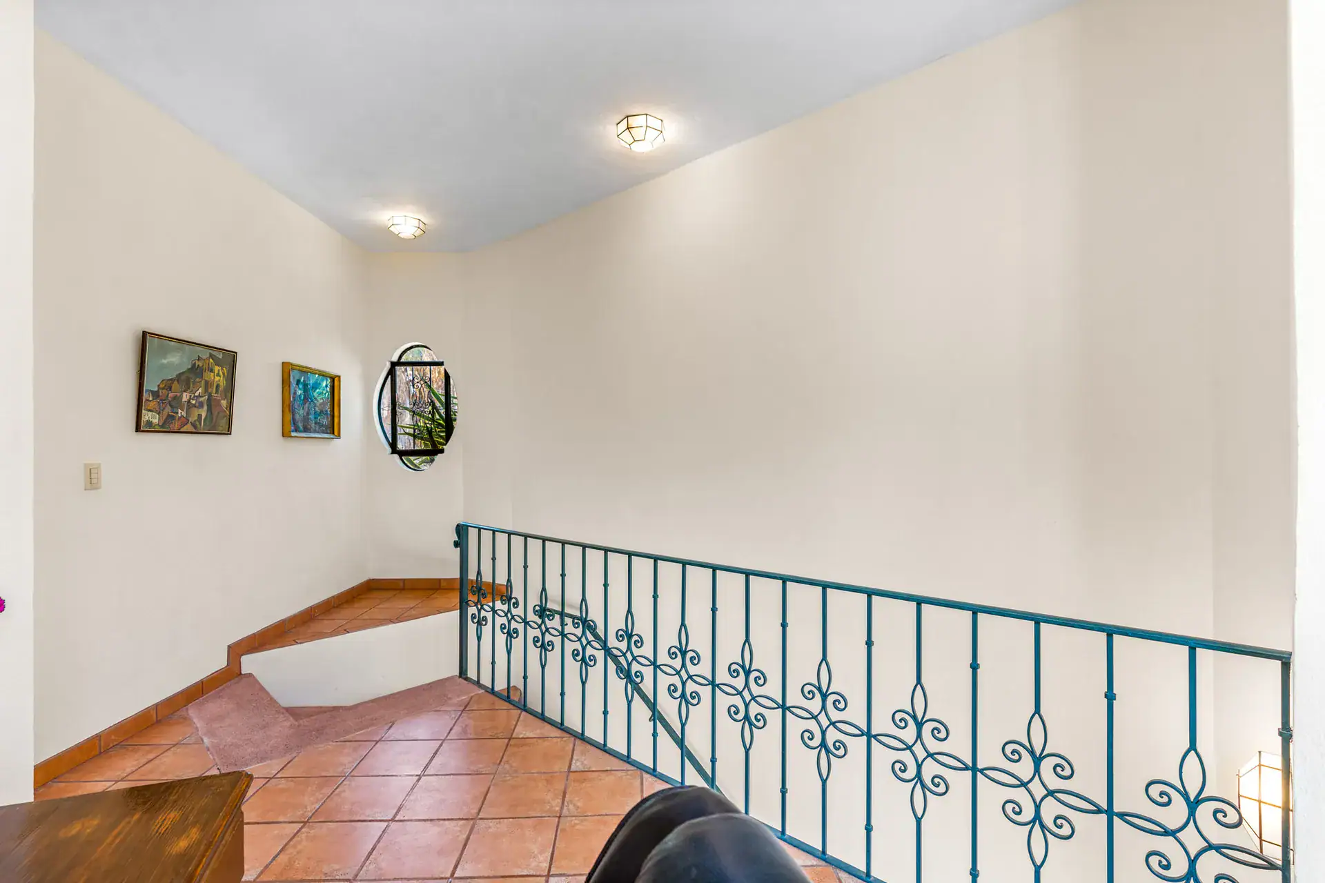 Casa Cul-De-Sac Armonia, upstairs alcove with a teal iron railing, paintings and a round window, San Miguel de Allende
