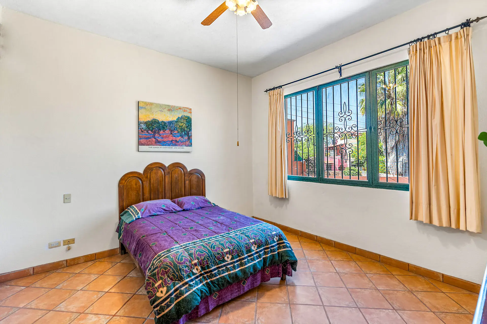 Casa Cul-De-Sac Armonia, bedroom with a carved wood headboard, a purple patterned bedspread, a window with curtains and a ceiling fan, San Miguel de Allende