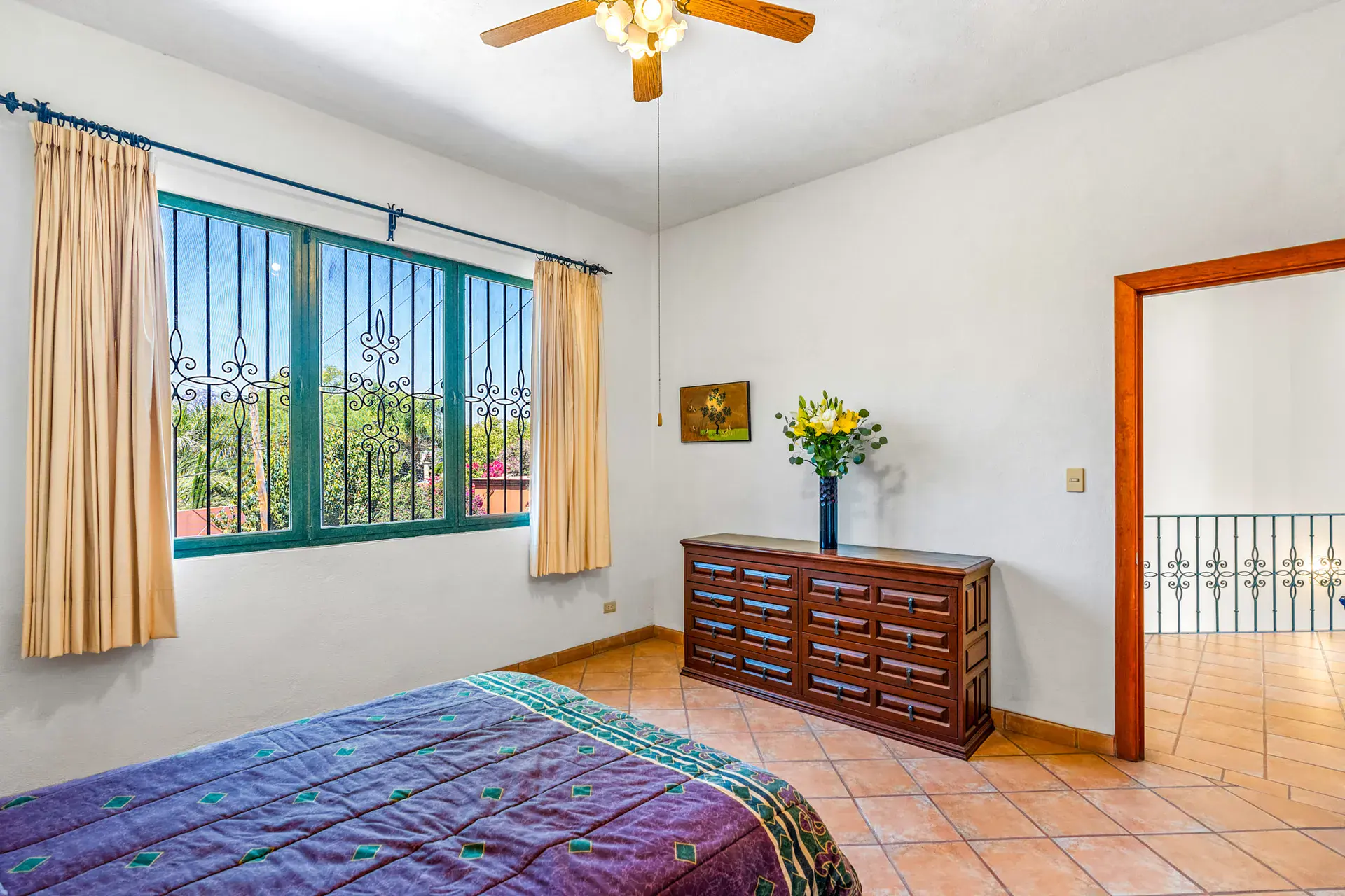 Casa Cul-De-Sac Armonia, bedroom with a purple bedspread, a wood chest of drawers, a window with curtains and a ceiling fan, San Miguel de Allende