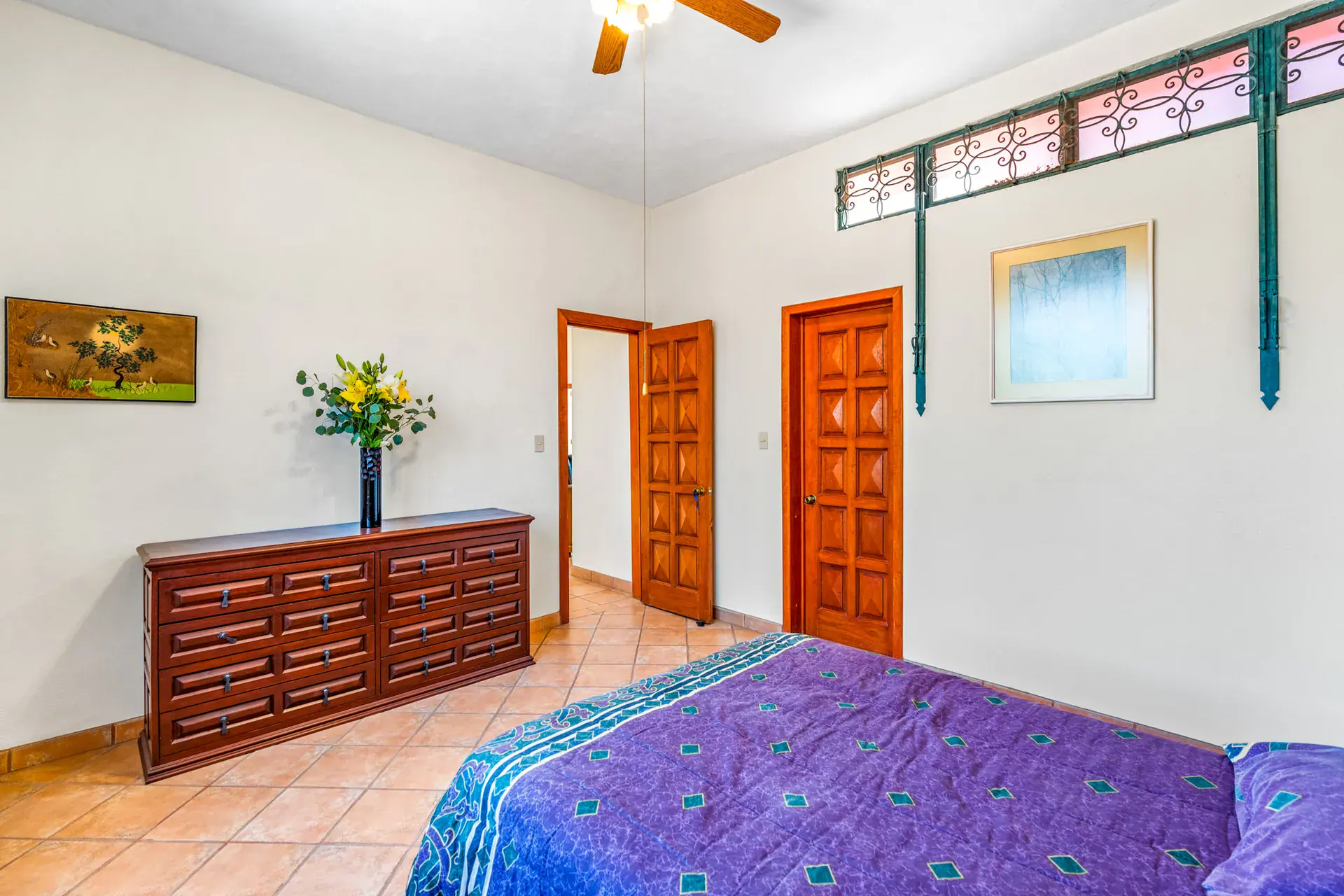 Casa Cul-De-Sac Armonia, bedroom with a purple bedspread, a wood chest of drawers, a transom window and a doorway to the landing, San Miguel de Allende
