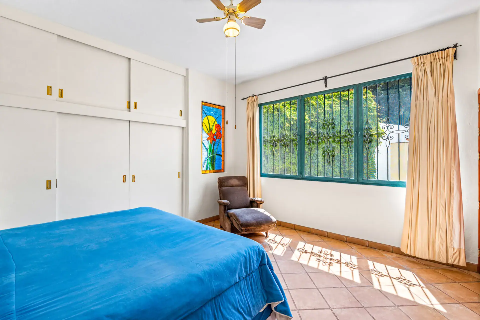 Casa Cul-De-Sac Armonia, bedroom with a blue bedspread, built-in wardrobes and a window with curtains onto a garden, San Miguel de Allende