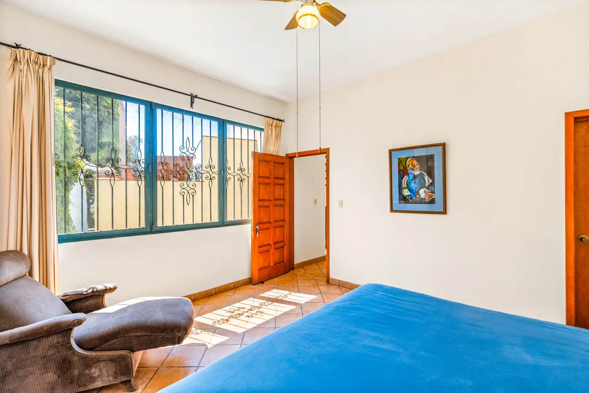 Casa Cul-De-Sac Armonia, bedroom with a blue bed, a ceiling fan, a lounge chair and a window with curtains, San Miguel de Allende
