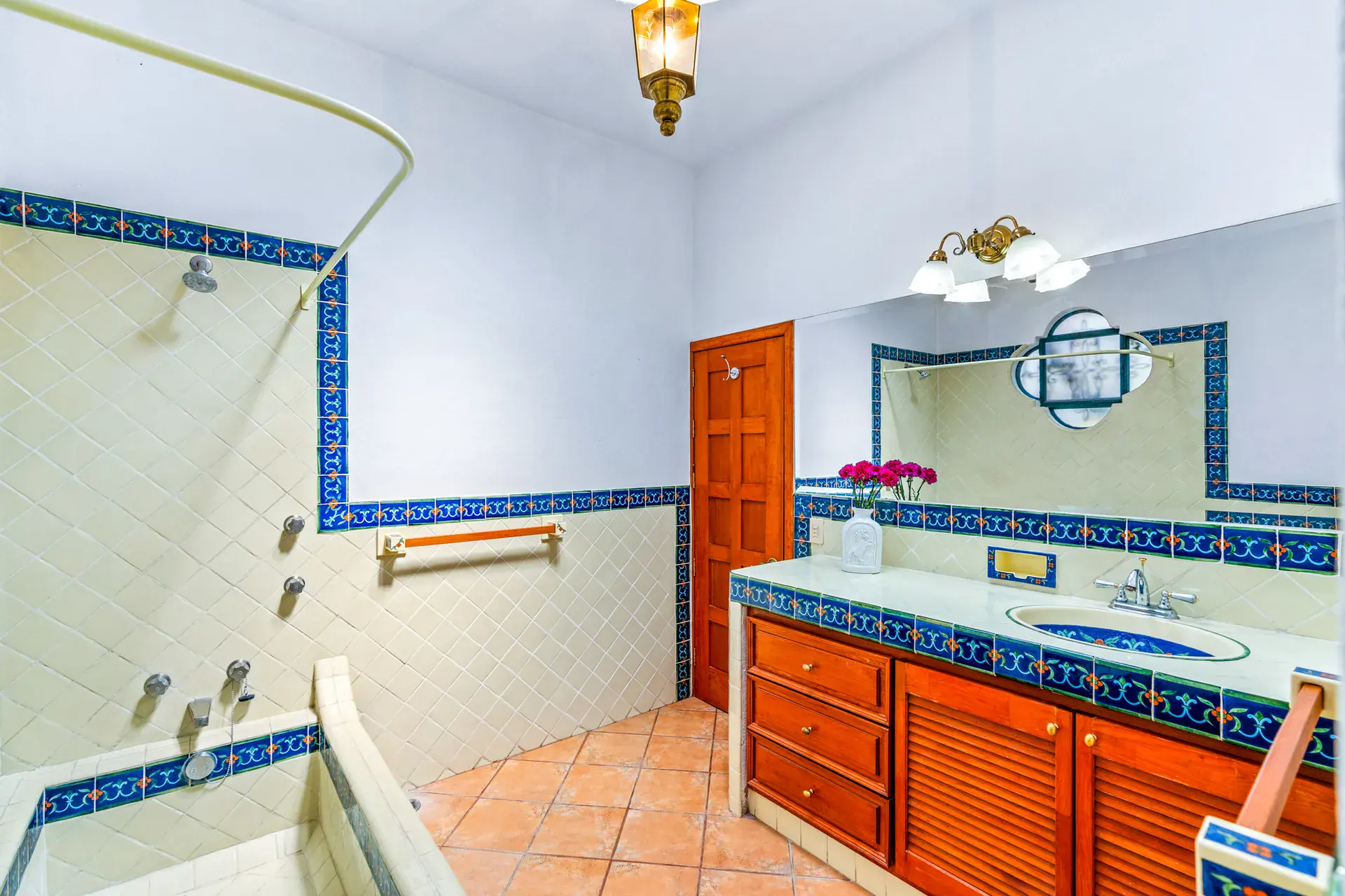 Casa Cul-De-Sac Armonia, bathroom with blue-bordered tile, a shower and bath, a vanity with wood cabinets and a round window, San Miguel de Allende