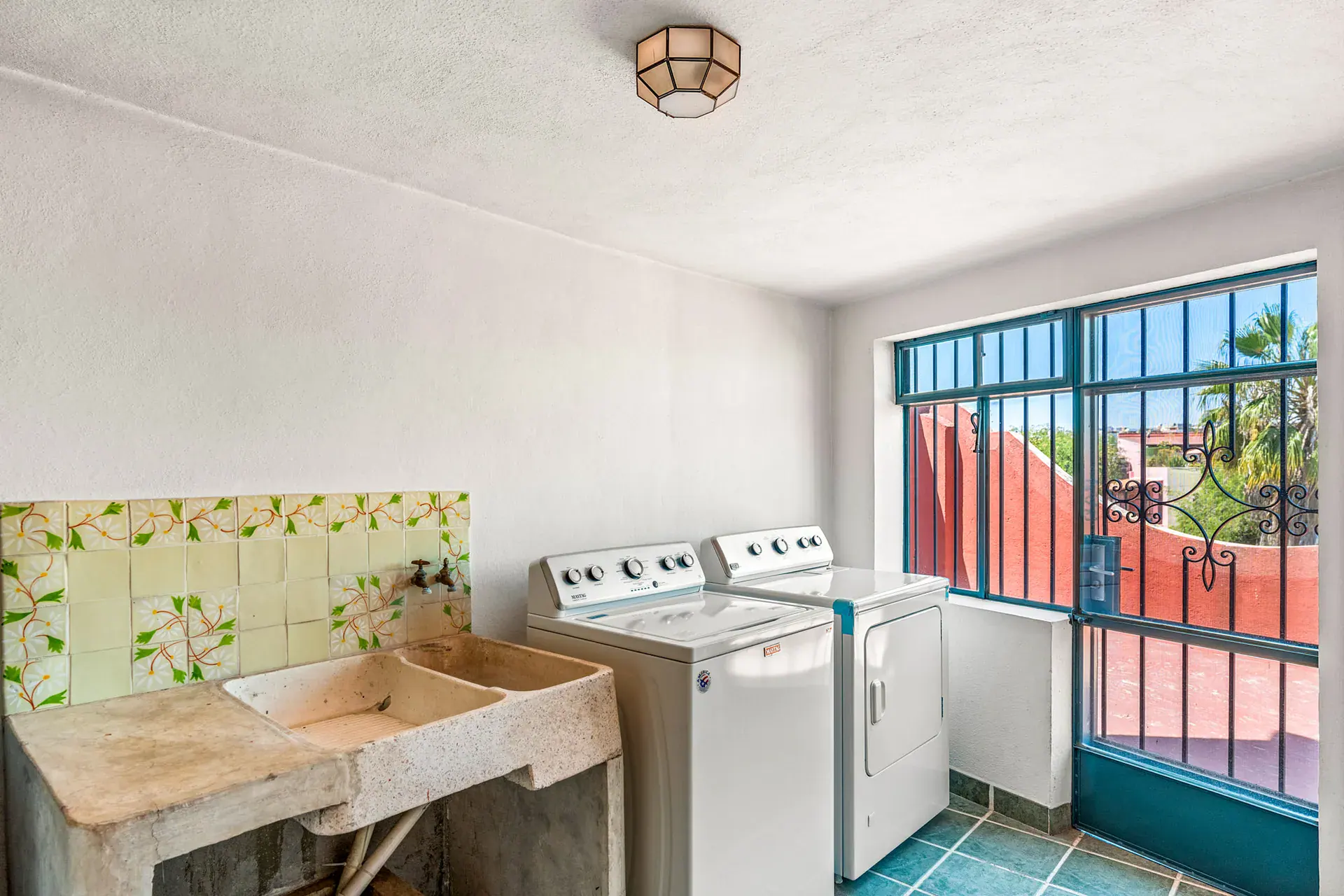 Casa Cul-De-Sac Armonia, laundry room with a washer and dryer, a stone sink, floral tile and a teal-framed barred door, San Miguel de Allende
