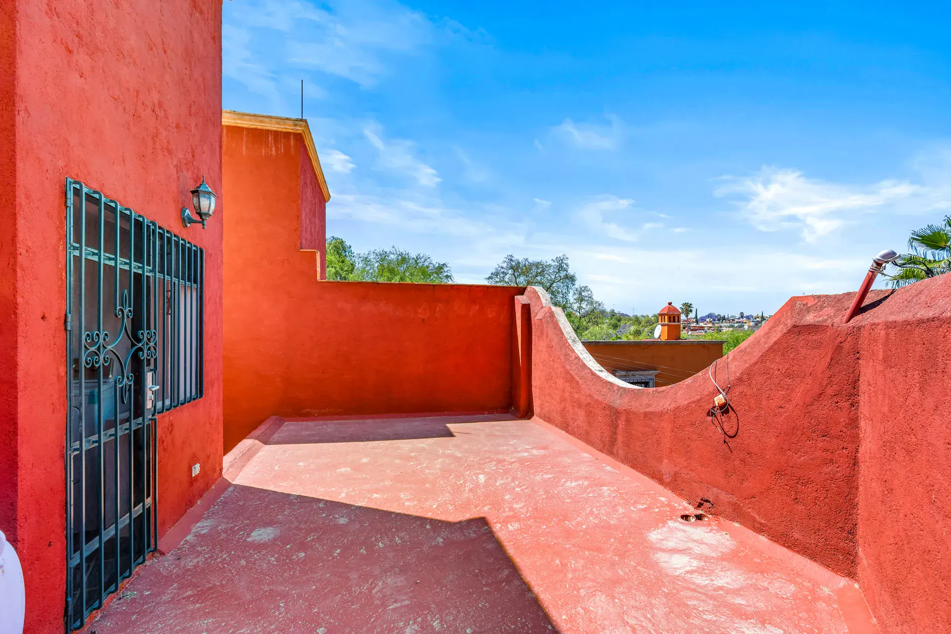 Casa Cul-De-Sac Armonia, red-walled roof terrace with a barred door and curved parapet wall, San Miguel de Allende