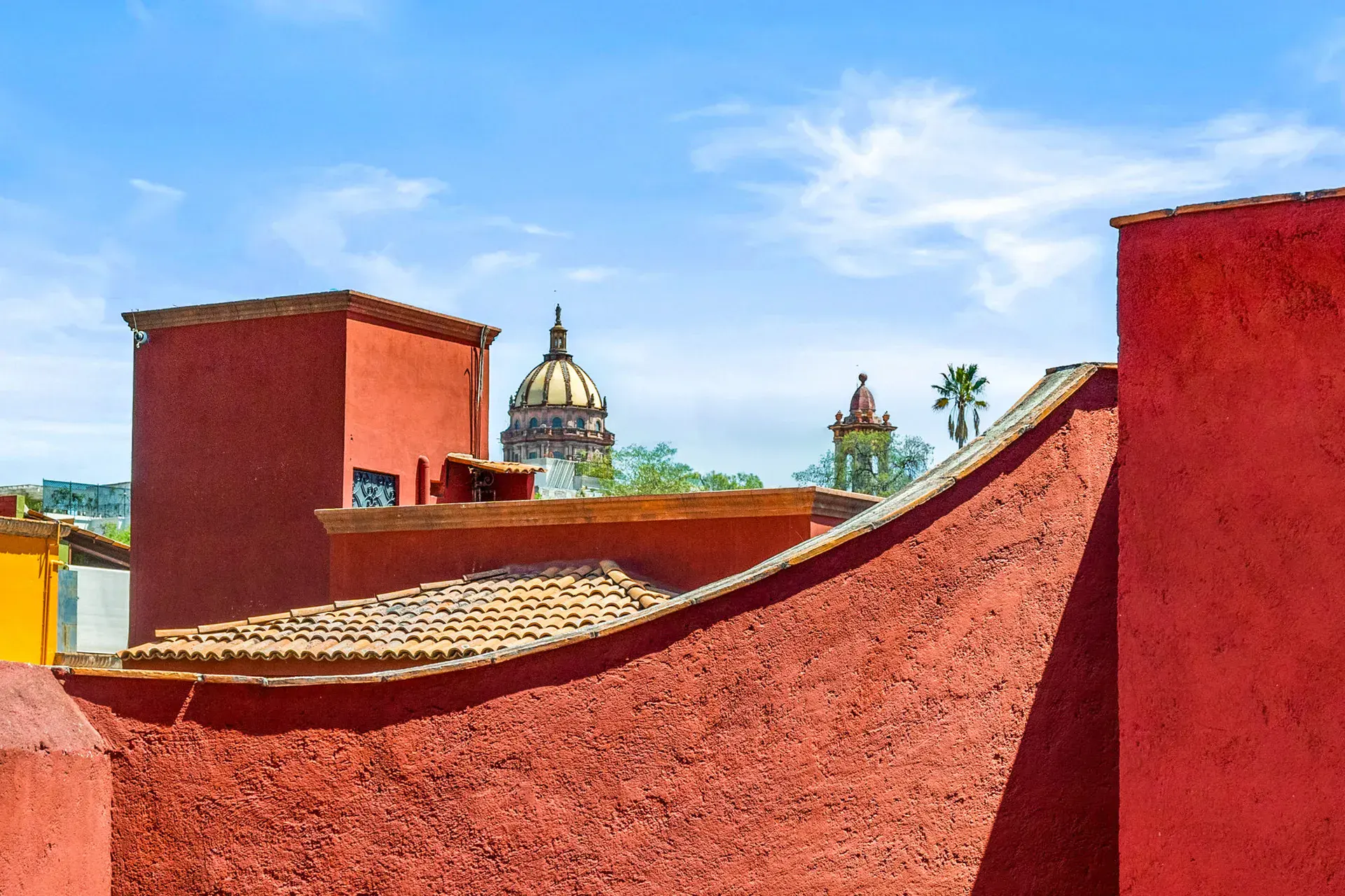 Casa Cul-De-Sac Armonia, roof terrace with a curved red parapet and a view of church domes, San Miguel de Allende