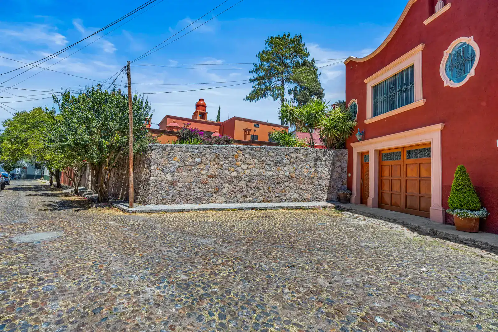 Casa Cul-De-Sac Armonia, red facade with a round window and a wood garage door beside a stone wall on a cobblestone cul-de-sac, San Miguel de Allende