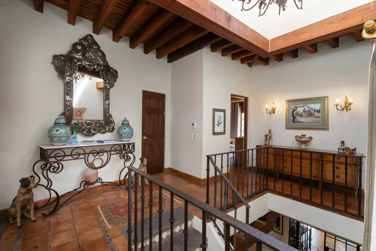 Casa de Gracia, upstairs landing with an ornate tin mirror on an iron console table and a wood-beam ceiling, San Miguel de Allende