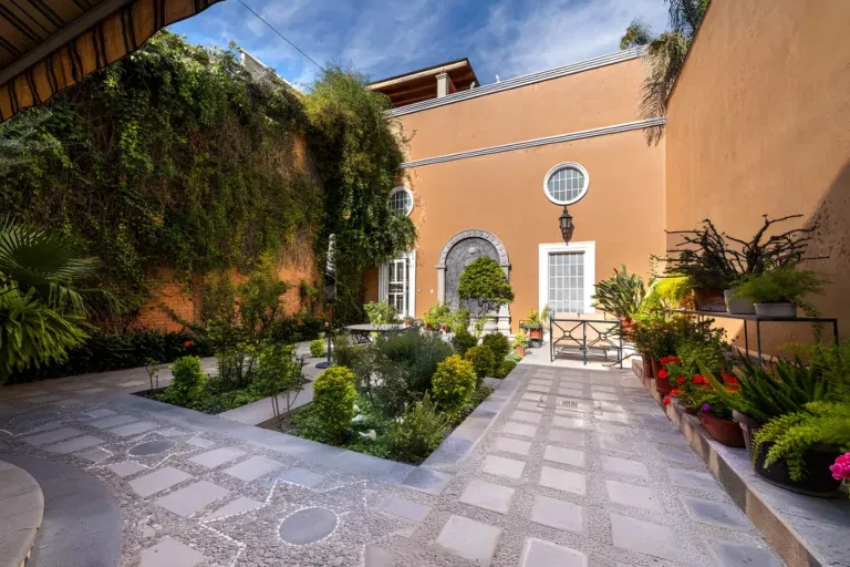 Casa de la Gracia, courtyard with a stone paver path, clipped hedges, flowering plants and an orange house wall, San Miguel de Allende