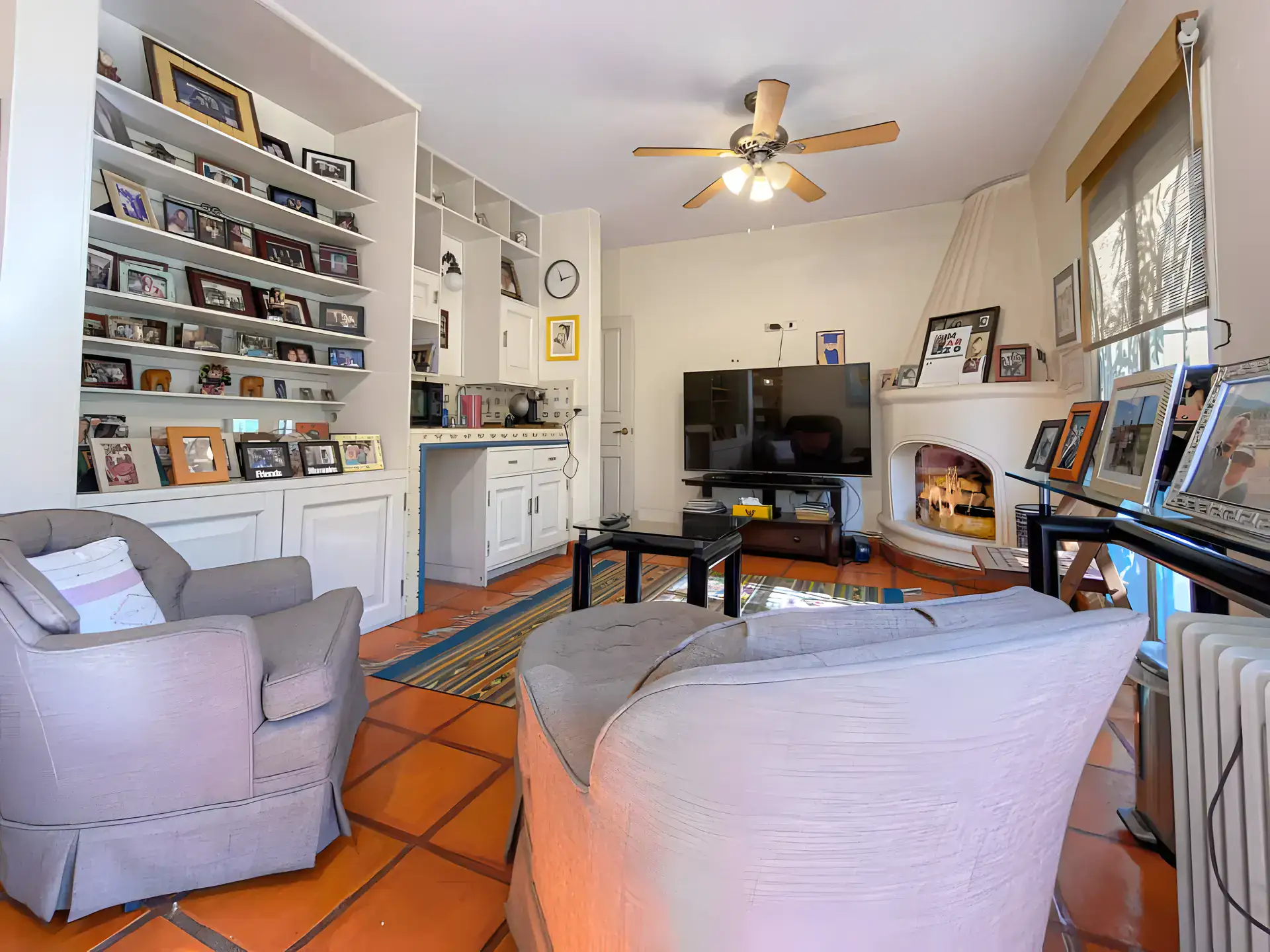Casa de la Gracia, family room with built-in photo shelves, a corner fireplace, gray armchairs and a television, San Miguel de Allende