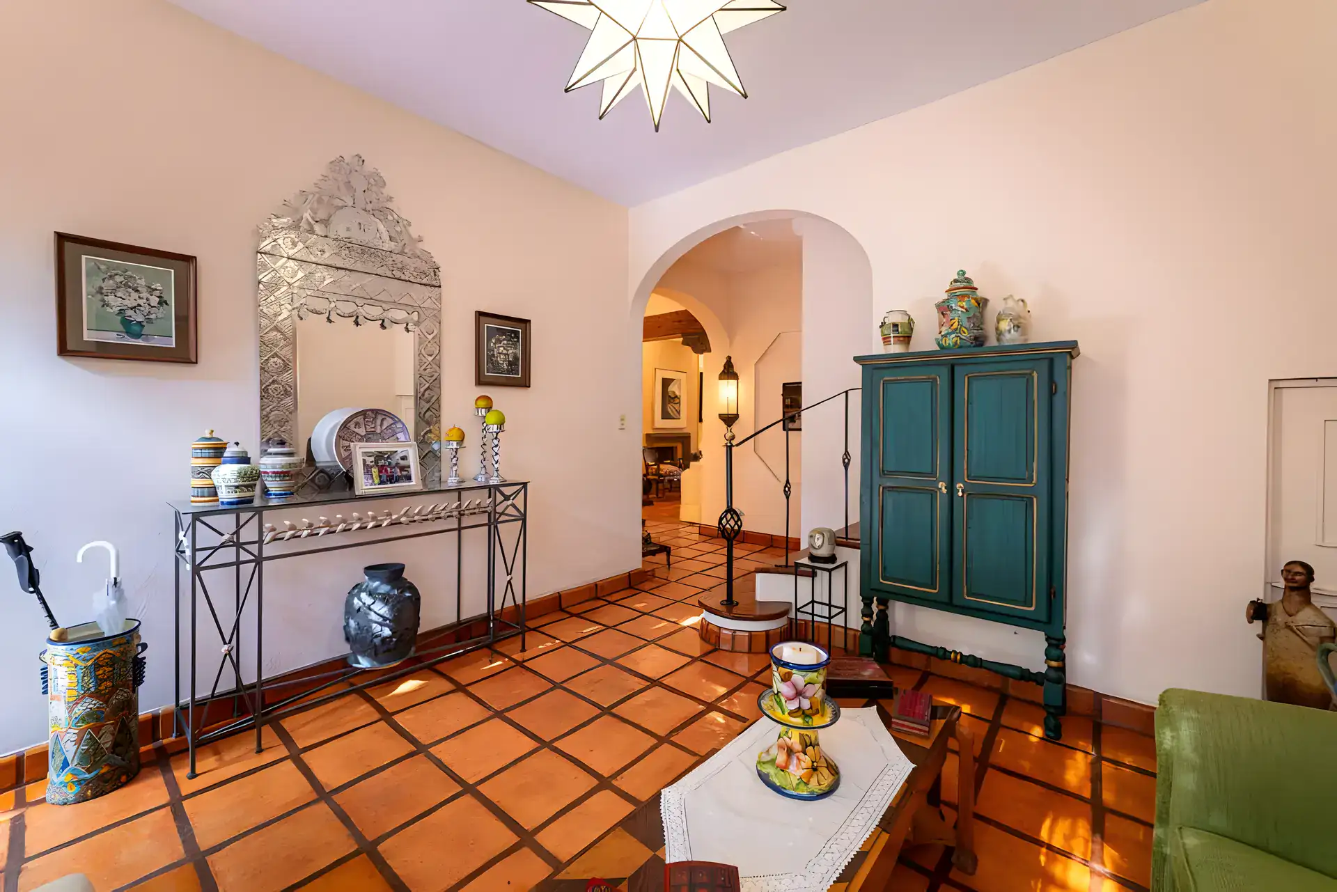 Casa de la Gracia, entry sitting room with a carved metal mirror, a console, a green armoire and a star lantern, San Miguel de Allende