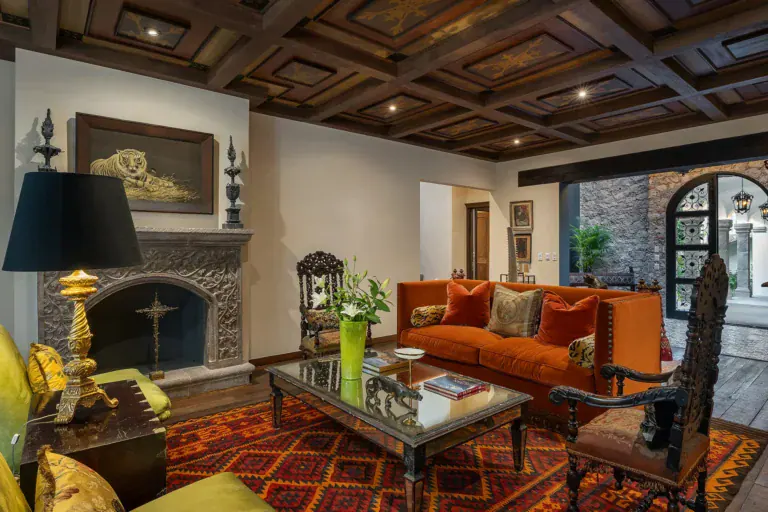 Casa de la Leona, living room with a stone fireplace, orange sofa and a coffered wood ceiling, San Miguel de Allende