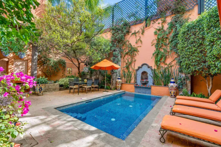 Casa de la Suerte, courtyard pool with an orange umbrella and loungers among flowers, San Miguel de Allende