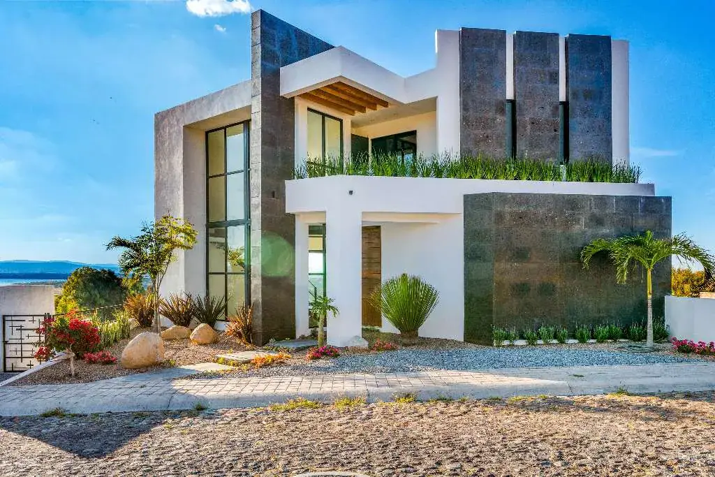 Casa de la Vista, modern white and dark stone house with tall glass windows and a green roof garden above a gravel street, San Miguel de Allende