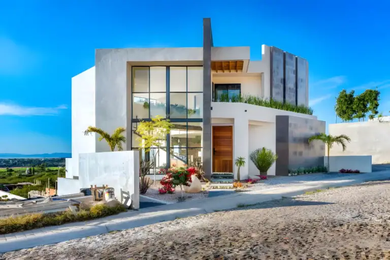 Casa de la Vista, corner view of the contemporary house with a wood front door, glass stair tower and desert plants, San Miguel de Allende
