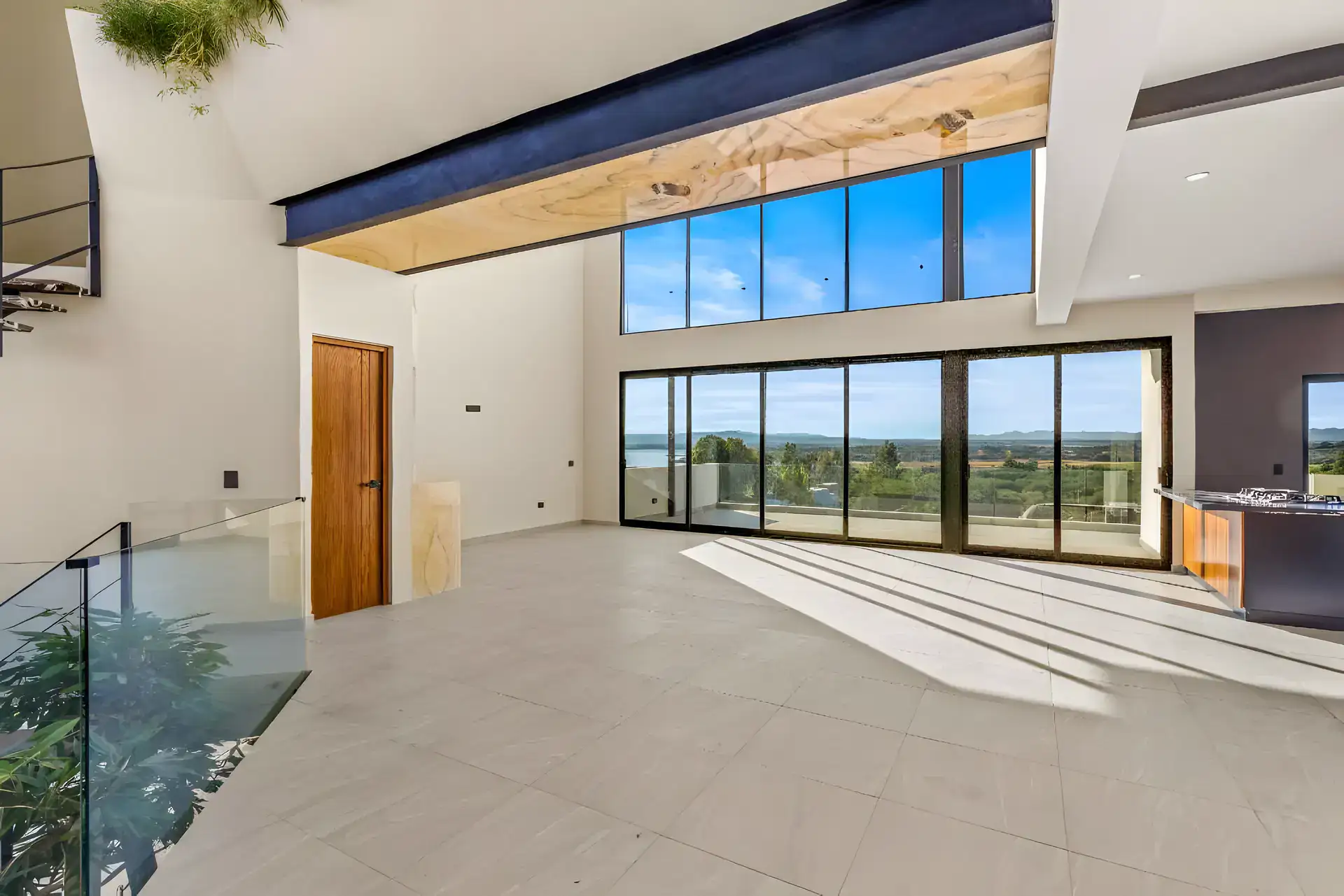 Casa de la Vista, unfurnished double-height living room with a glass railing and a wall of glass doors facing the valley, San Miguel de Allende