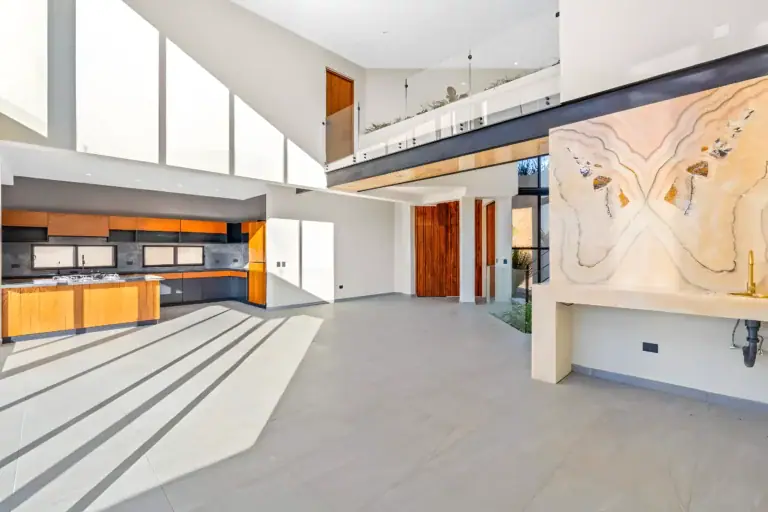 Casa de la Vista, unfurnished open-plan living, kitchen and dining area with a glass-railed mezzanine and a glowing onyx wall, San Miguel de Allende