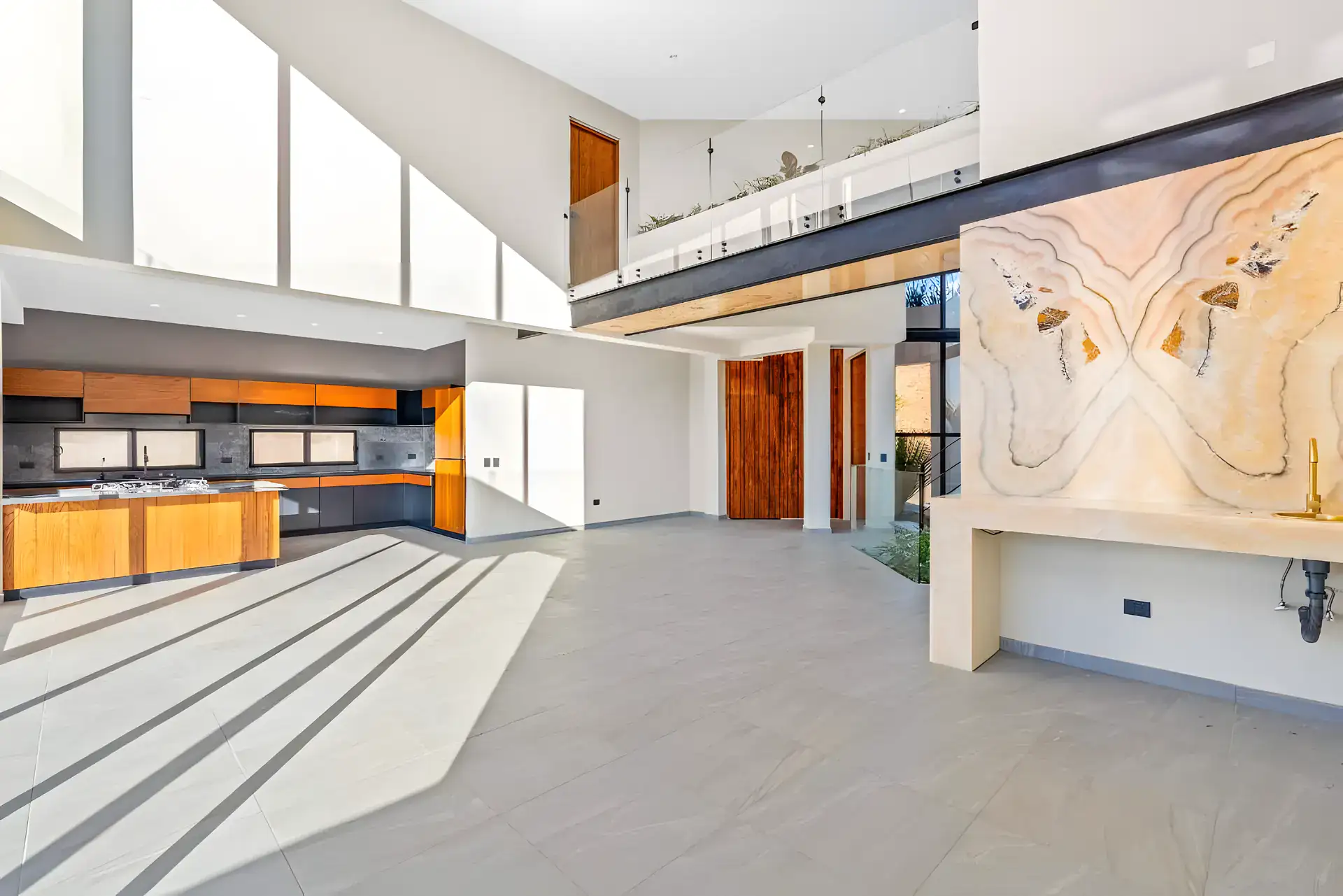 Casa de la Vista, unfurnished open-plan living, kitchen and dining area with a glass-railed mezzanine and a glowing onyx wall, San Miguel de Allende