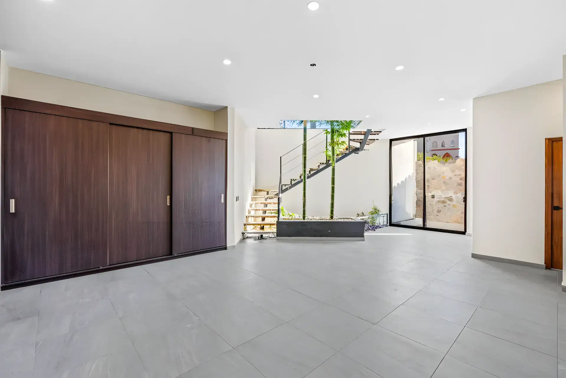 Casa de la Vista, empty room with a dark wood sliding wardrobe, a floating stair with a bamboo planter and a glass wall, San Miguel de Allende